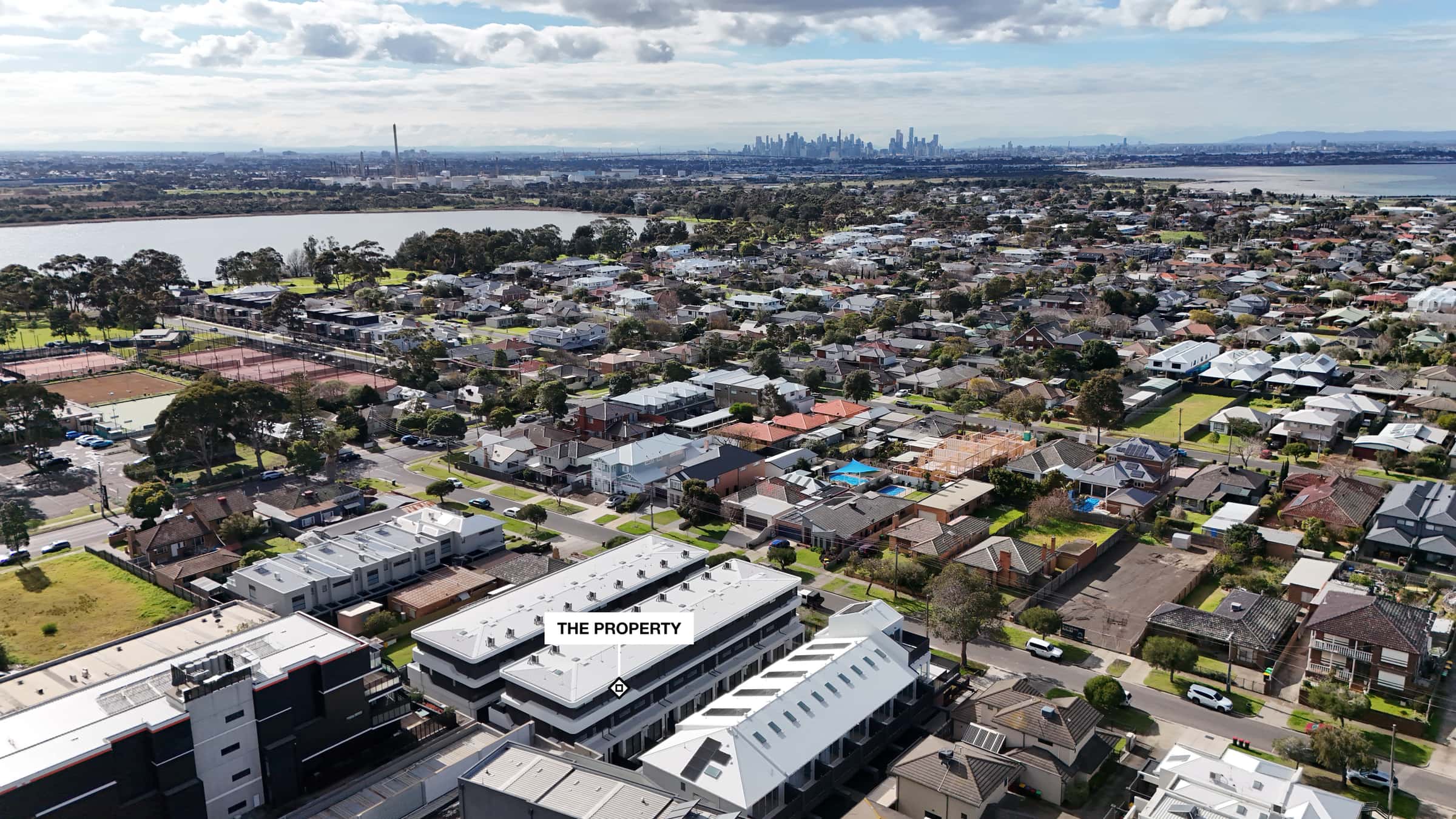 A real pinned photo from the Pin the Lot engine: our own drone photo of a bayside Melbourne street, the property marked by a plate reading THE PROPERTY, no place pins on this single frame, the lake and the city skyline behind it.